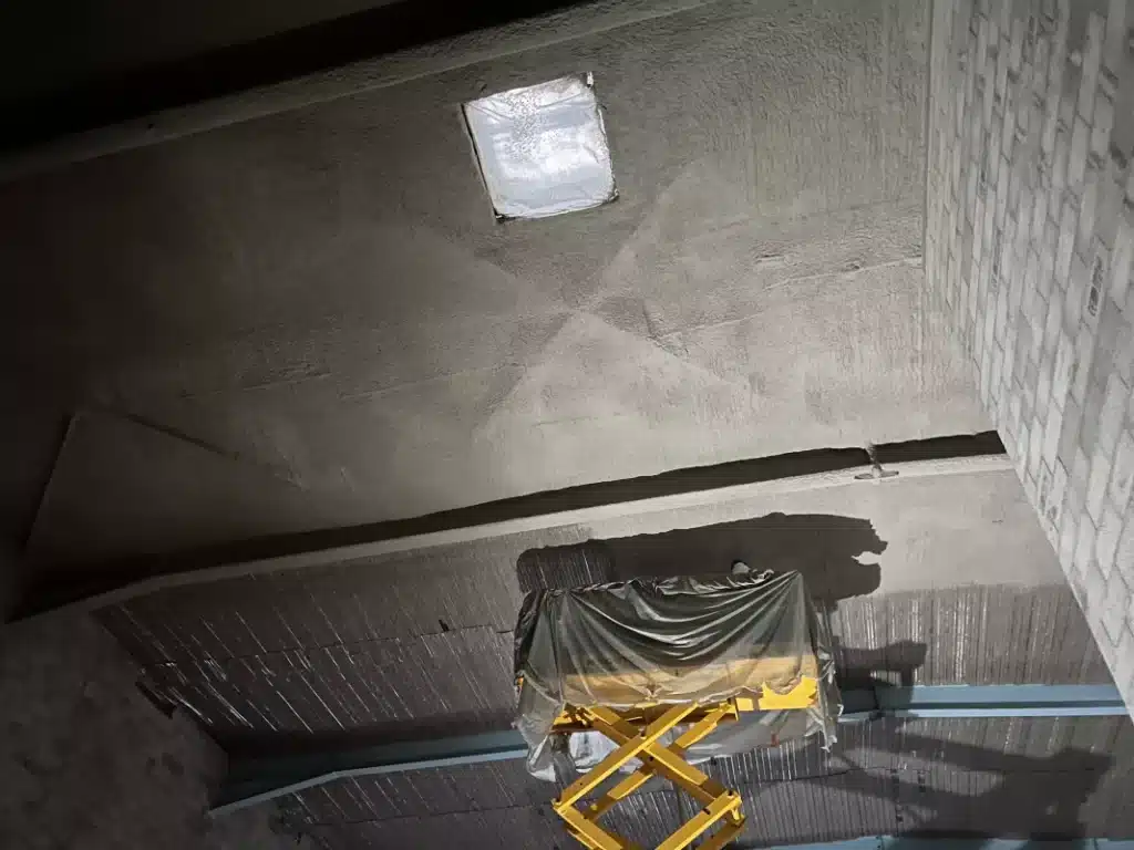 Application d’enduit pâteux projeté sur un plafond en béton dans le cadre d’une solution de protection incendie pour bâtiment industriel.